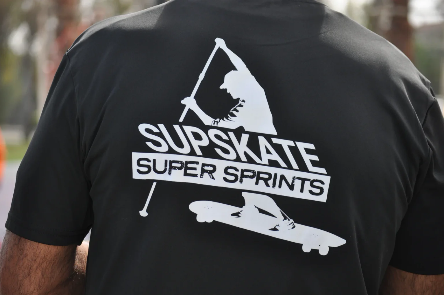 Dettaglio di una maglietta nera con la scritta SUPSkate Super Sprints e una grafica bianca di un praticante su tavola