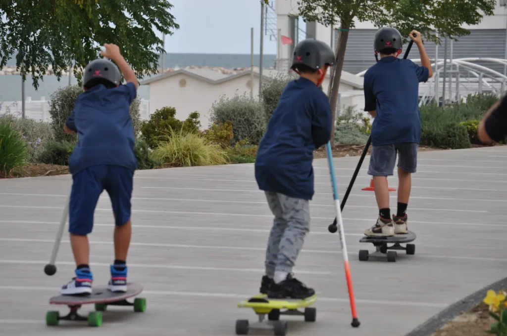 Tre ragazzi con casco praticano SUPSkate su tavole a ruote utilizzando bastoni da spinta.