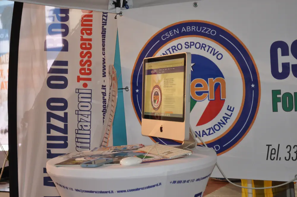 Postazione informativa CSEN Abruzzo On Board con computer, materiale associativo e logo CSEN durante un evento.