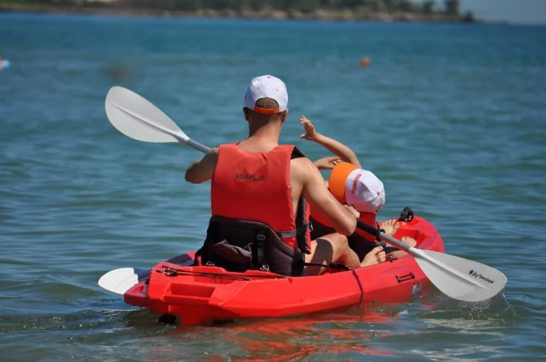 Adulto e bambino con giubbotti salvagente arancioni su un kayak rosso mentre pagaiano in mare