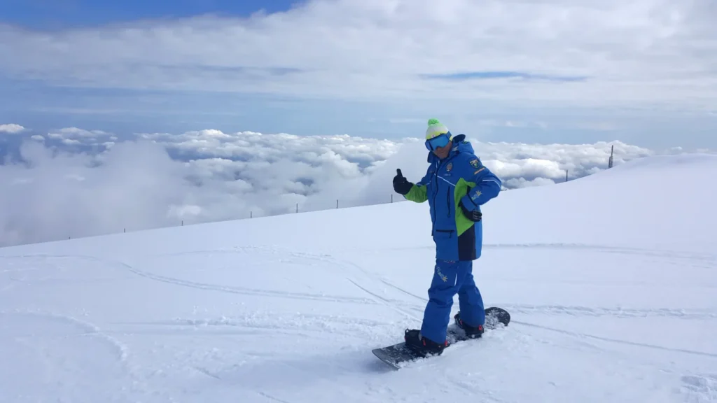 Maestro federale di snowboard con abbigliamento blu e verde sulla neve, con una distesa di nuvole sullo sfondo