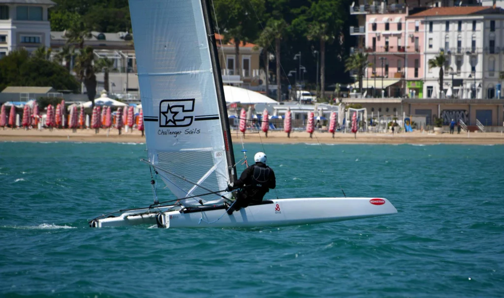 Velista con casco bianco al trapezio su un catamarano Classe A davanti alla spiaggia di Vasto Marina