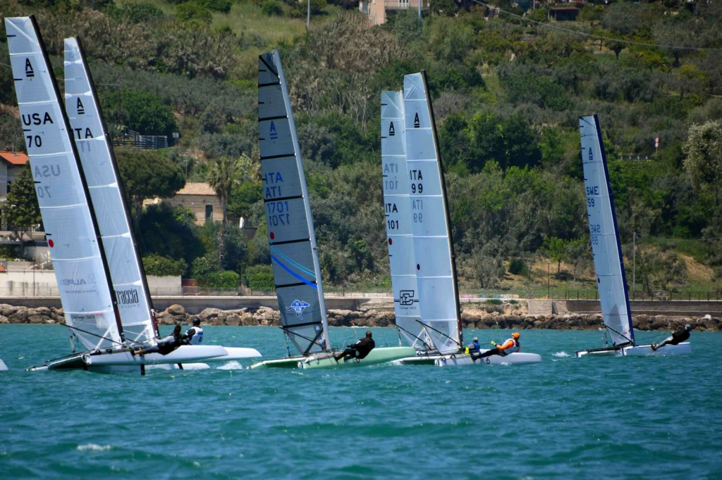Catamarani Classe A in regata a Vasto Marina con velisti al trapezio e costa alberata sullo sfondo