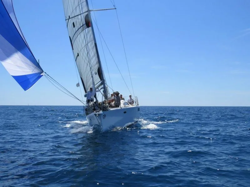 Barca a vela con spinnaker e equipaggio in navigazione in mare aperto