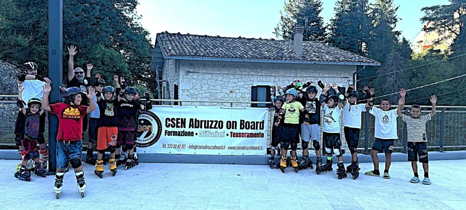 Gruppo di bambini con pattini in linea, caschi e medaglie al collo alza le braccia insieme a un adulto durante la premiazione finale