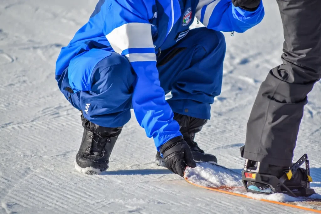 Maestro Federale di Snowboard con divisa nazionale blu mostra un dettaglio della tavola a un praticante sulla neve