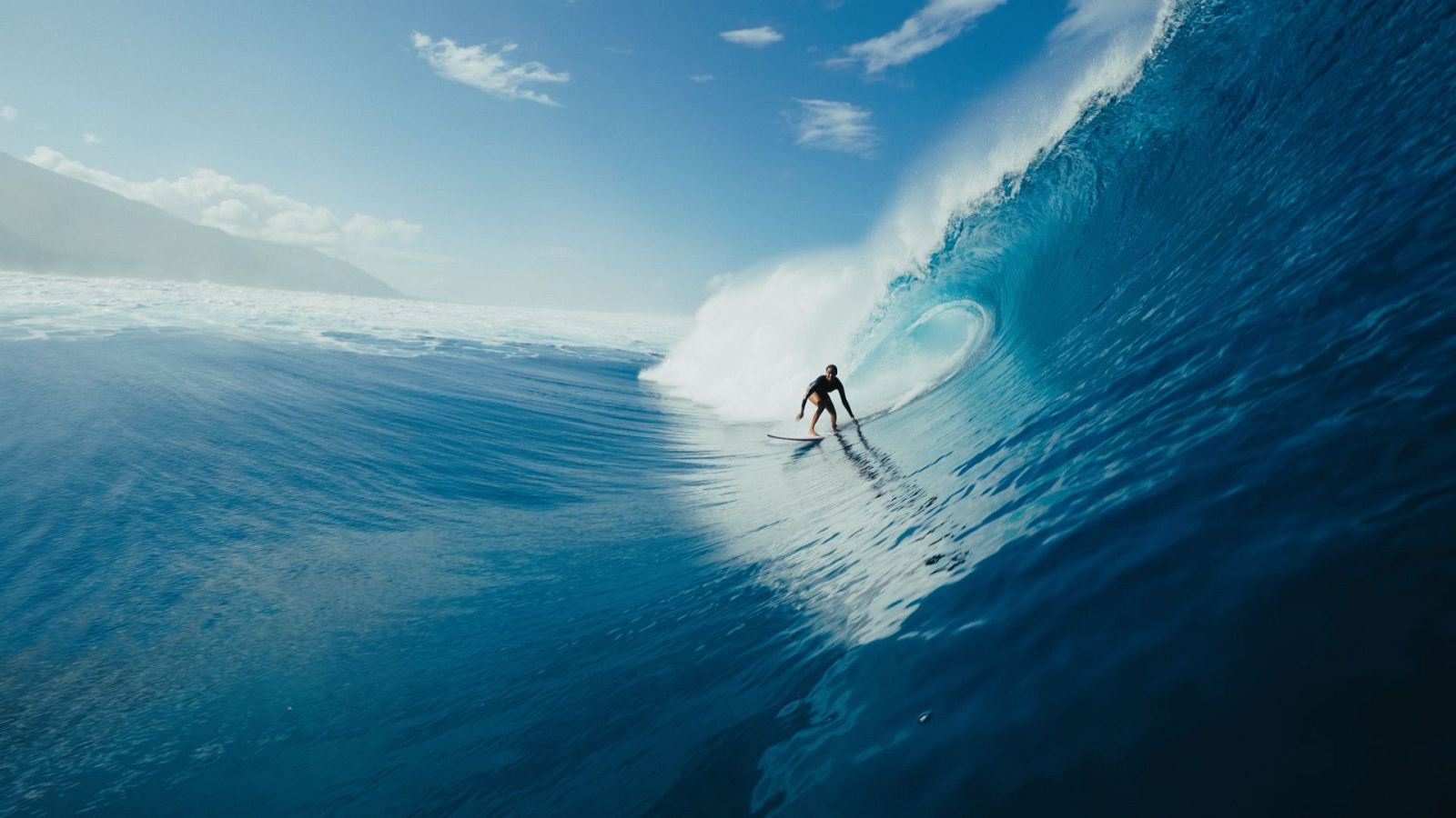 Surfista sulla parete di una grande onda blu mentre si avvicina alla sezione tubante